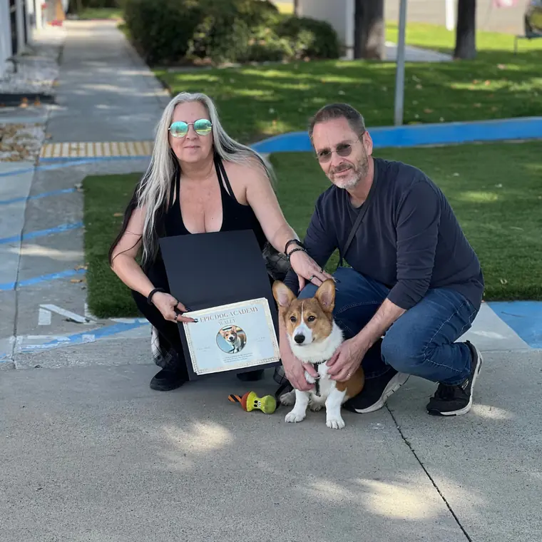 A couple kneeling with their corgi and his Epic Dog Academy diploma