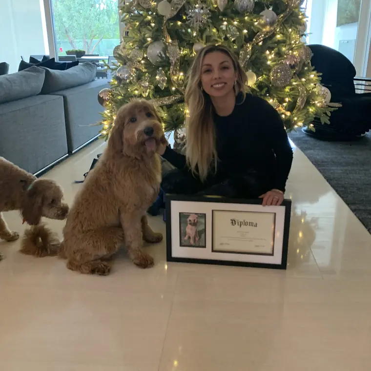 A dog owner at home with her two doodles and their Epic Dog Academy diploma